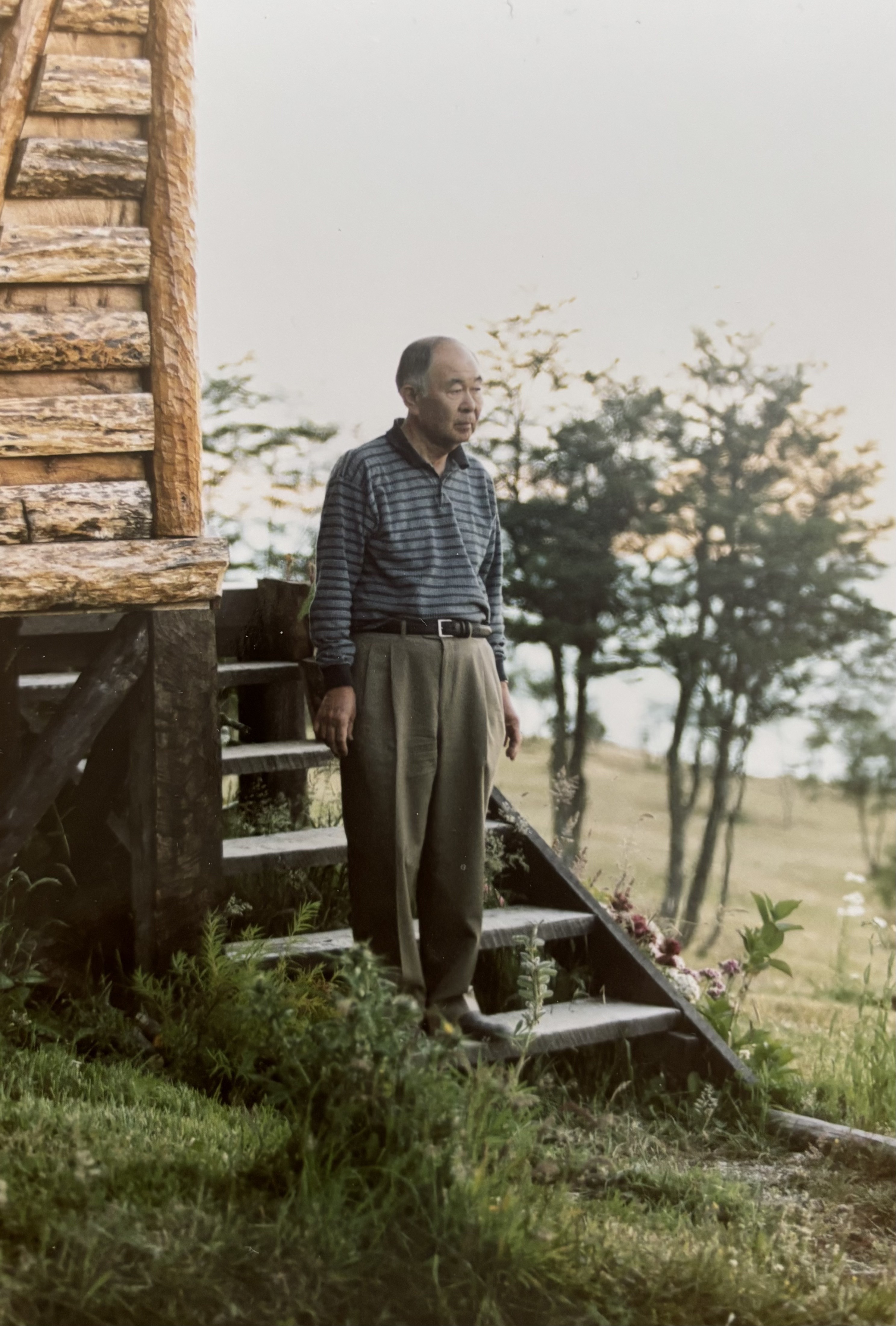 Our grandfather standing on the steps of a wooden cabin, backlit in the evening light.
